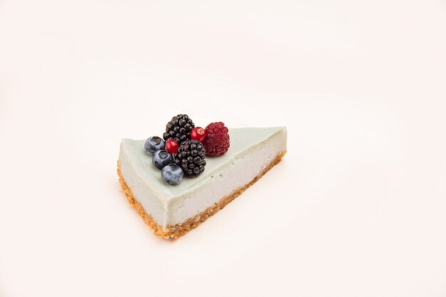 Side view of blue cheesecake with different berries on it isolated over white