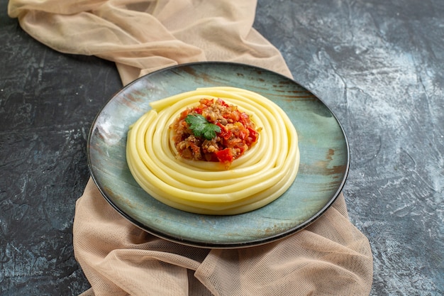 Вид сбоку на синюю тарелку с вкусной пастой, подаваемой с помидорами и мясом на полотенце коричневого цвета