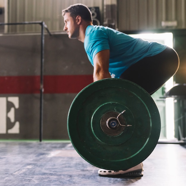 Side view bodybuilding concept with strong man raising barbell