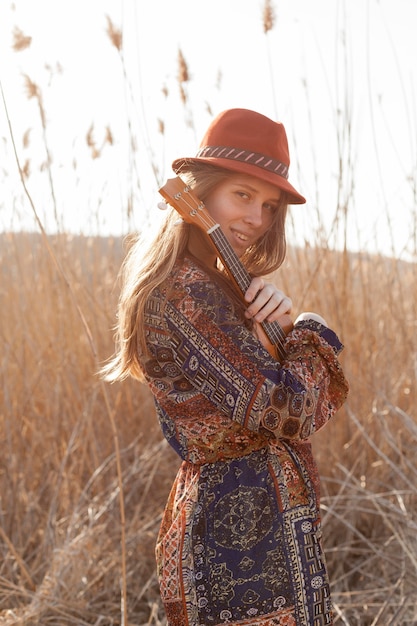 Free photo side view of bohemian woman posing in the field with ukulele