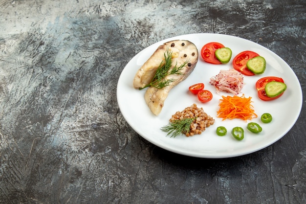 Side view of boiled fish buckwheat served with vegetables green on a white plate on ice surface