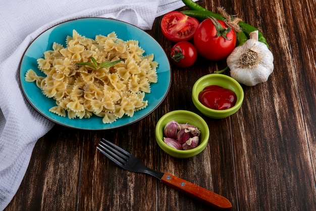 Side view of boiled pasta on a blue plate with a fork tomatoes ketchup and chili peppers on a wooden surface