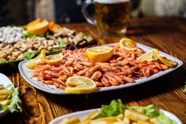 Side view boiled shrimp with lemon wedges on a plate with beer snacks and a glass of beer on the table
