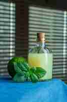 Free photo side view bottle of lemon juice with leaves and green lemon on black window surface. vertical copy space for text