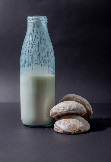 Free photo side view of bottle of milk and cookies on black surface