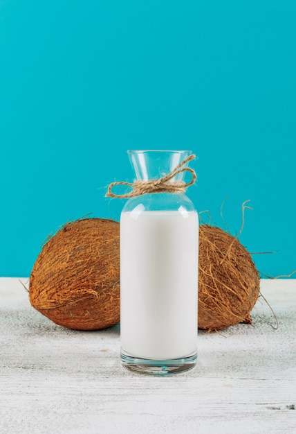 Bottiglia di latte di vista laterale con le noci di cocco su fondo di legno bianco. orizzontale