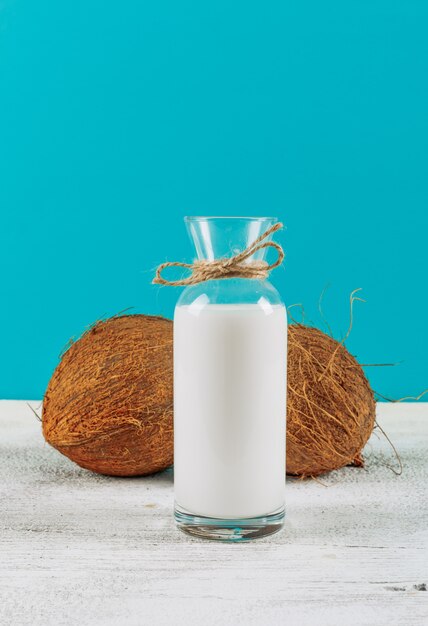 흰색 나무 바탕에 코코넛 우유의 측면보기 병. 수평