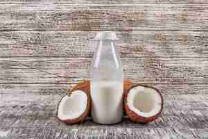 Free photo side view bottle of milk with divided in half coconuts on gray wooden background. horizontal