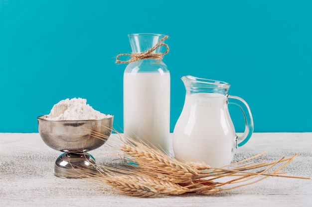 小麦粉のボウルに牛乳の側面ビューボトル、白い木製と青い布の背景に小麦。横型