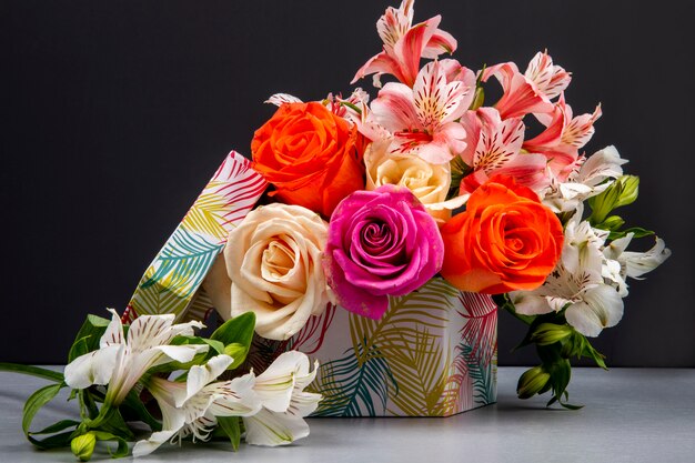 Side view of a bouquet of colorful roses and pink color alstroemeria flowers in a gift box on black table