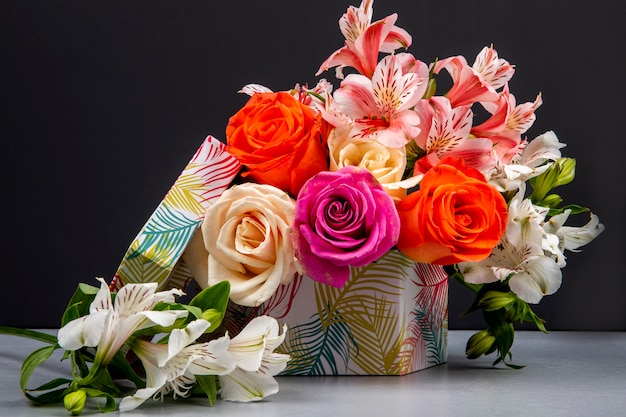 Side view of a bouquet of colorful roses and pink color alstroemeria flowers in a gift box on black table