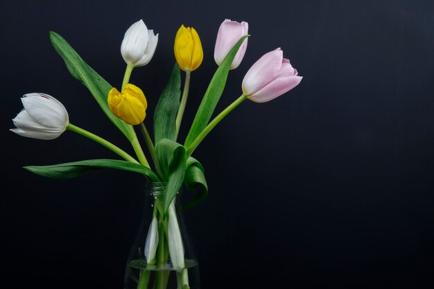 Вид сбоку букет из разноцветных тюльпанов цветы в стеклянной бутылке на черном фоне
