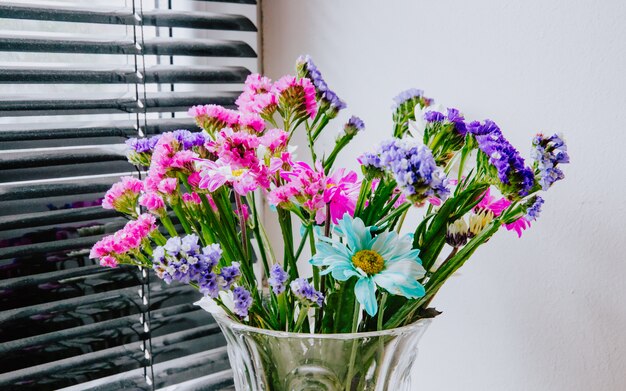 Free photo side view of a bouquet of pink white purple and blue color statice and chrysanthemum flowers in a glass vase at white wall background