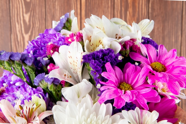 Side view of a bouquet of pink white and purple color statice alstroemeria and chrysanthemum flowers in craft paper isolated at rustic background