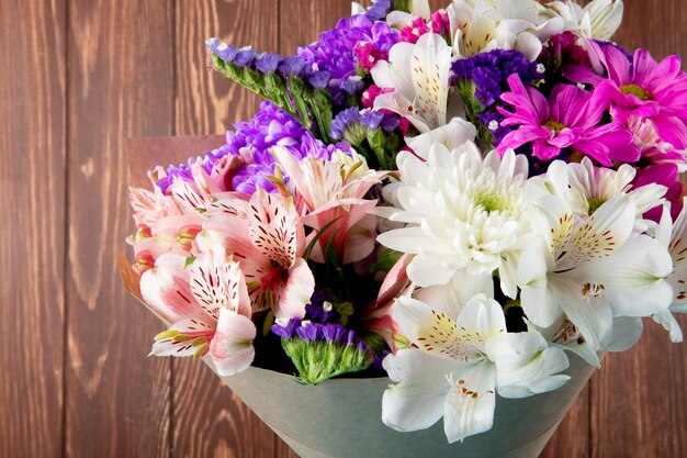 Side view of a bouquet of pink white and purple color statice alstroemeria and chrysanthemum flowers in craft paper isolated on rustic background