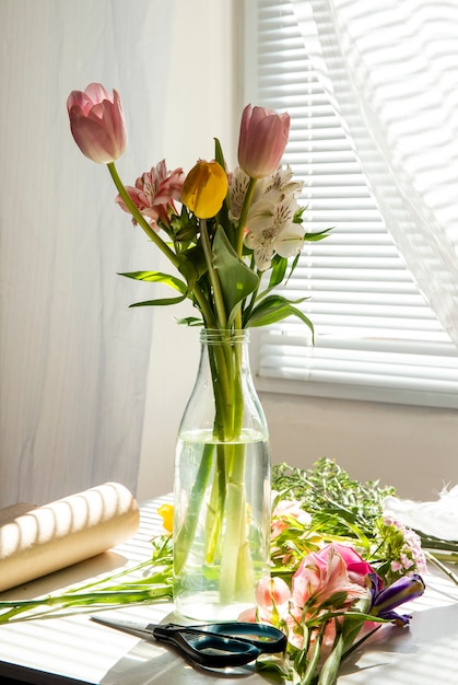 Вид сбоку букета розовых и желтых цветных тюльпанов с цветами альстромерии в стеклянной бутылке на столе