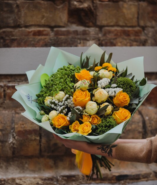 Side view of bouquet of yellow color roses white color peonies eustomas and trachelium wall flowers on brick wall wall