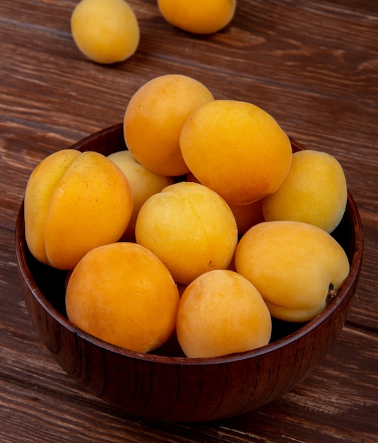 Side view of bowl of apricots on wooden background