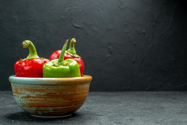 Free photo side view of bowl of bell peppers on the left side on dark grey table with dark green background