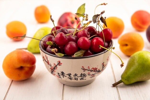 Side view of bowl of cherries with pattern of fruits as peach and pear on wooden background