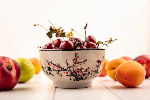 木製の表面と白い背景に桃と梨のような果物のパターンを持つサクランボのボウルの側面図