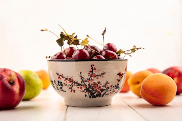 Side view of bowl of cherries with pattern of fruits as peach and pear on wooden surface and white background