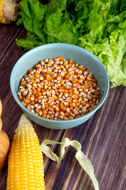 Side view of bowl of corn seeds with corn and lettuce on wooden table