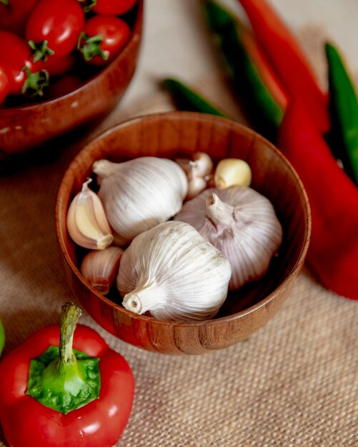 Side view of bowl full of garlic with other vegetables on sackcloth surface