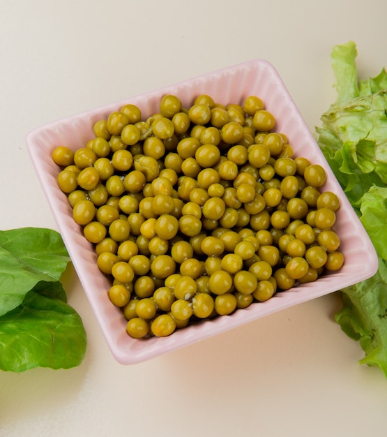 Side view of bowl full of green pea with spinach and lettuce on white table