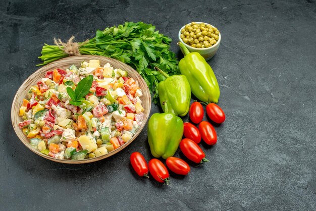 Side view of bowl of vegetable salad with vegetables on side on dark grey background