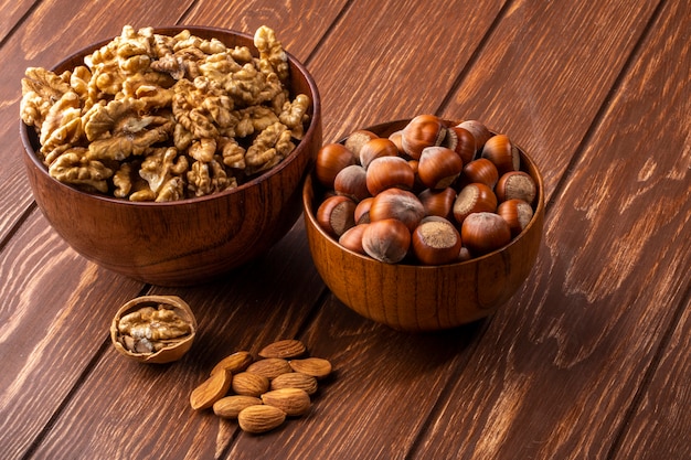 Side view bowl with inshell hazelnuts with a bowl of walnuts and almonds on the table