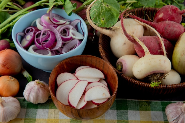 Side view of bowls and basket of vegetables as radish onion and garlic on cloth surface