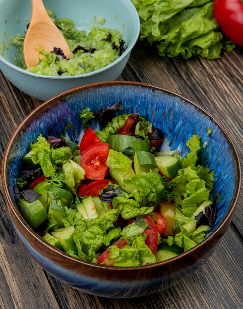 Side view of bowls of vegetable salads with wooden spoon lettuce tomato on wooden table