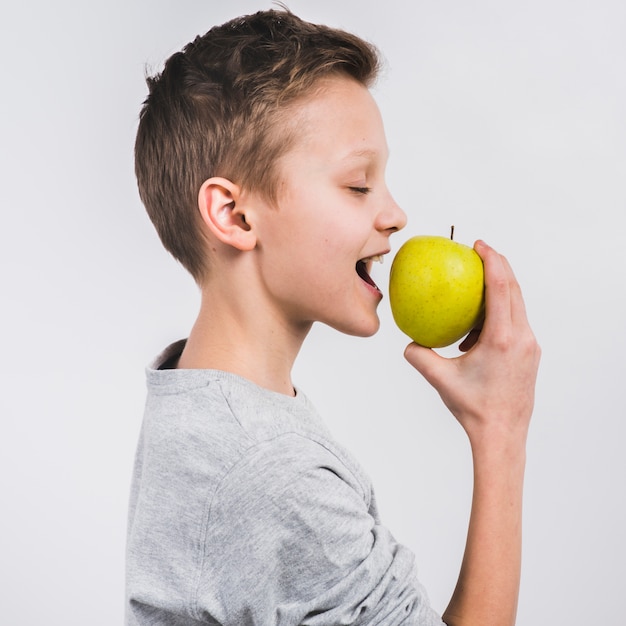Side view of a boy eating green fresh apple isolated on white background
