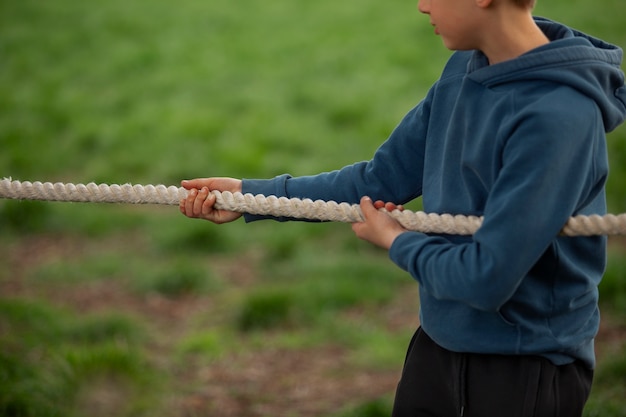 Free photo side view boy playing tug-of-war in the park