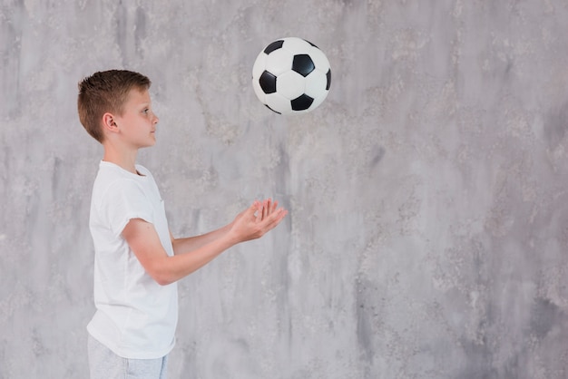 Side view of a boy playing with soccer ball against concrete backdrop