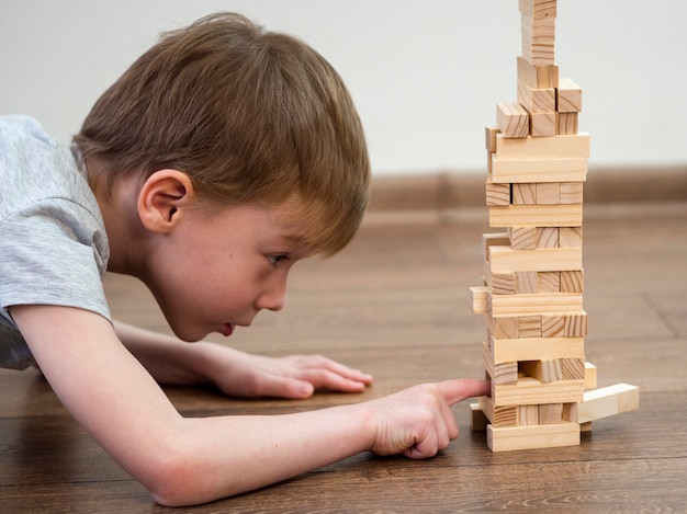 Free photo side view boy playing with wooden tower game