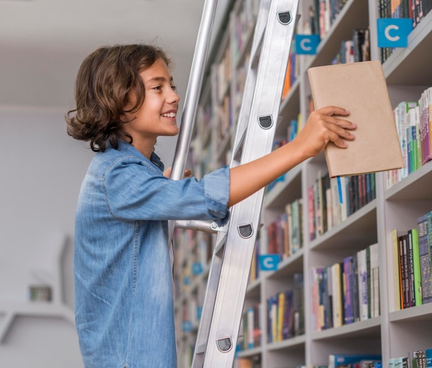 Side view boy putting back a book on the shelf