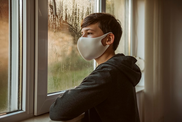 Side view boy with face mask looking through the window