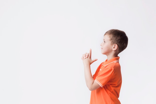 Side view of boy with gun gesture playing against white background