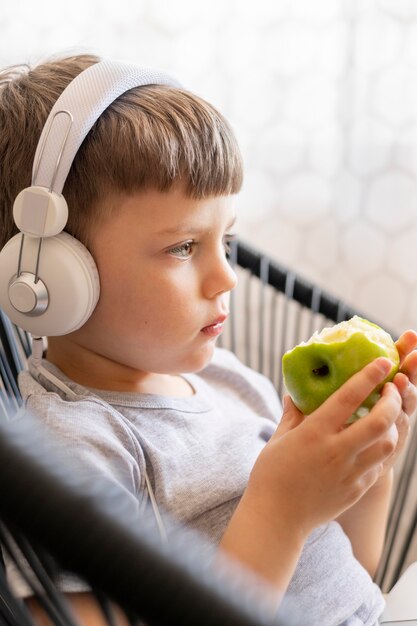 Side view boy with headphones eating apple