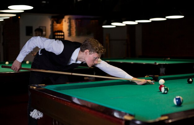 Side view boy with vest playing billiard 