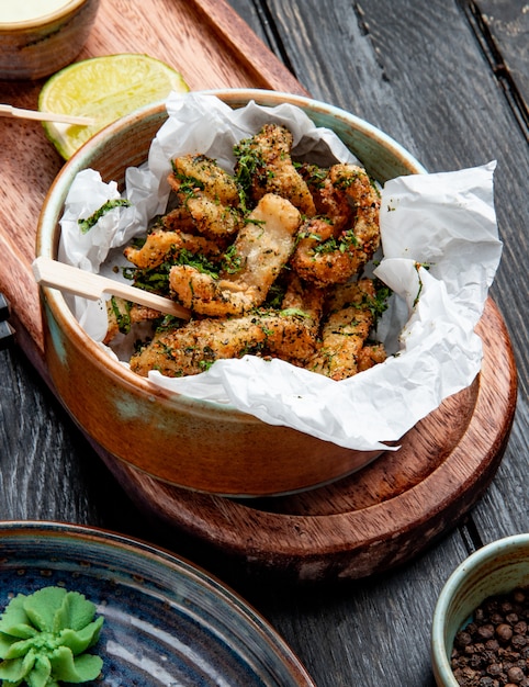 Foto gratuita vista laterale del pollo impanato con le erbe in una ciotola con la salsa di crema e del limone sul bordo di legno su rustico