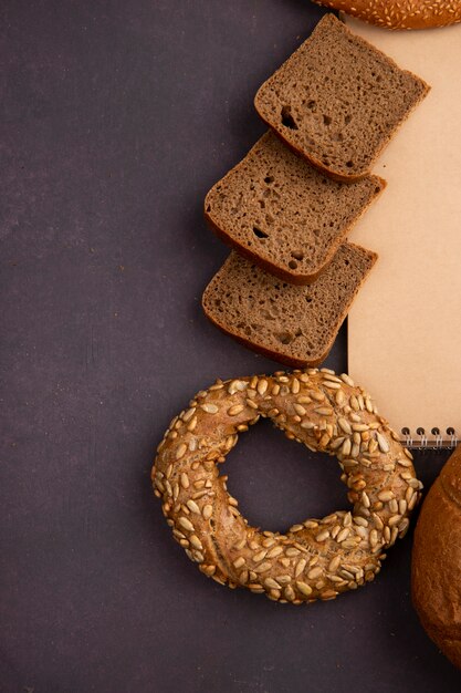 Side view of breads as bagel and rye bread slices on maroon background with copy space