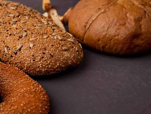 Side view of breads as bagel sandwich bread and classic cob on maroon background with copy space