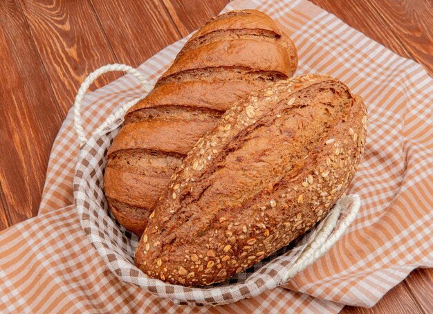 Side view of breads as black and seeded baguette in basket on plaid cloth and wooden surface
