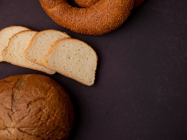 Side view of breads as classic cob white bread slices and bagel on maroon background with copy space