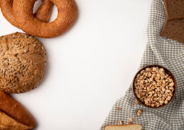 Side view of breads as cob bagel baguette rye with bowl full of corns on cloth on white background with copy space