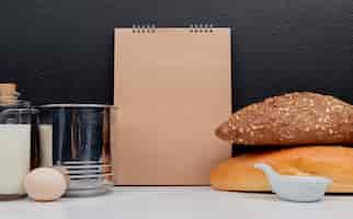 Free photo side view of breads as seeded  black and vietnamese baguette with egg butter sieve cup and note pad on white surface and black surface with copy space