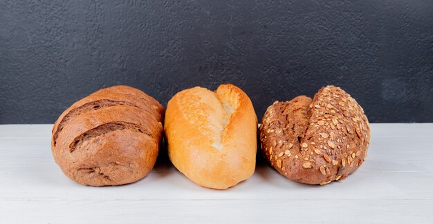 Side view of breads as seeded black and white vietnamese breads and black bread on wooden surface and black surface with copy space